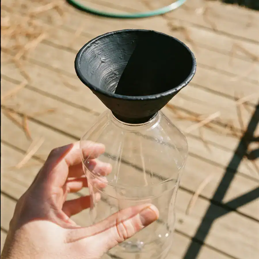Matte black painted plastic bottle funnel held above a weathered wooden deck in high-contrast sunlight.