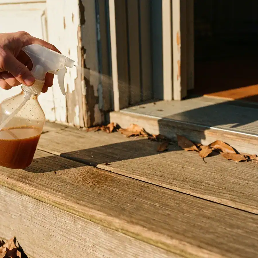 Close-up of a spray bottle misting essential oils onto weathered wooden porch steps near a textured door frame.