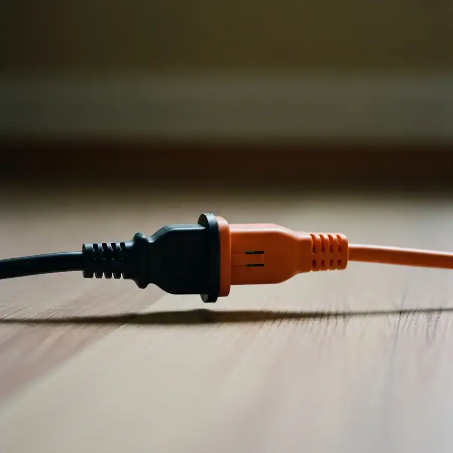 Close-up of a ZappBug heater's power cord plugged into a heavy-duty extension cord on a dusty floor for indoor safety.